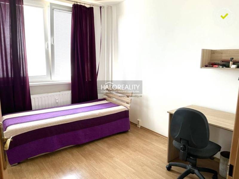 Room: bed with a purple blanket, desk, black chair, window with purple curtains.