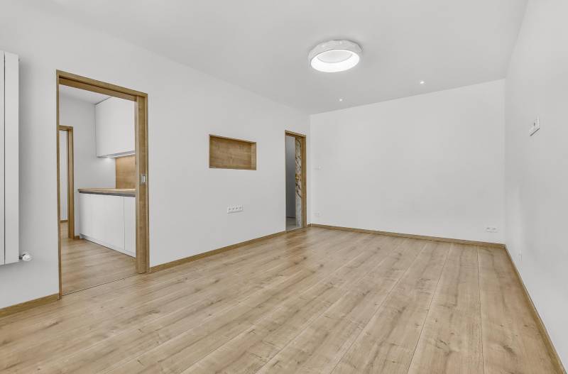 Spacious living room with wooden flooring and entrance to the kitchen in a 4-room apartment.