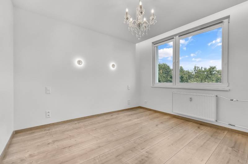 An empty room with a wooden floor, a chandelier, and a large window, 4-room apartment.