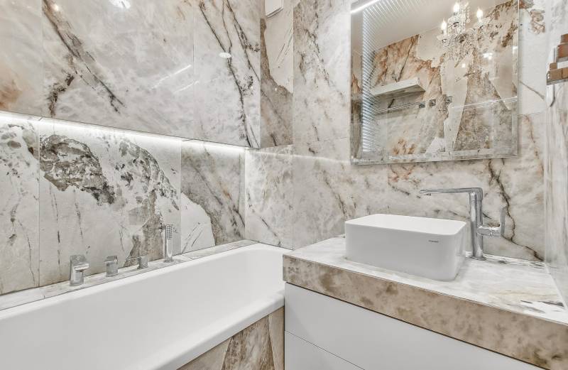 A bathroom in a 4-room apartment with a bathtub and a sink surrounded by marble tiles.