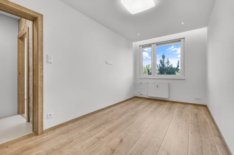An empty room with a wooden floor and a plastic window in a 4-room apartment.