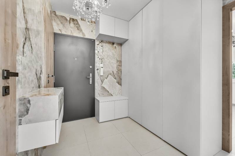 The hallway of a 4-room apartment with white furniture, textured walls, and a chandelier.