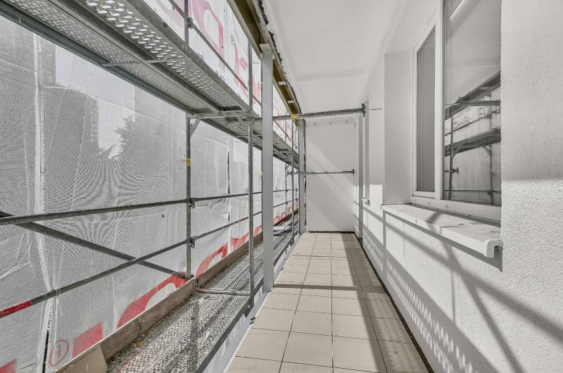 A balcony of a 4-room apartment under renovation with scaffolding and tiles.