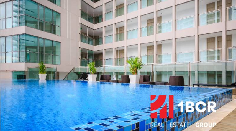 A swimming pool under construction in a residential complex in Pattaya, surrounded by glass buildings and lounge chairs.