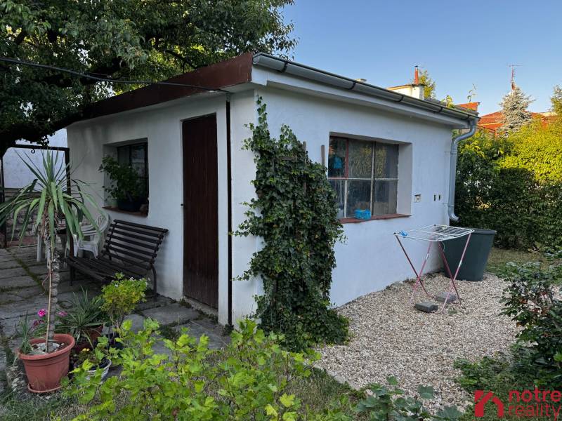 A family house in Lučenec with a garden house surrounded by greenery and a bench.