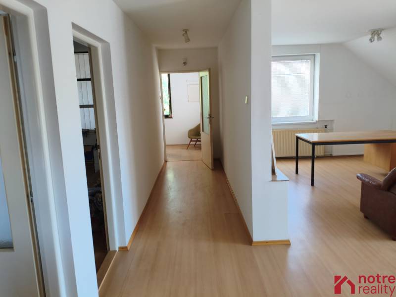 A hallway with a wooden floor, rooms on the left, a room with a table on the right in a family house.