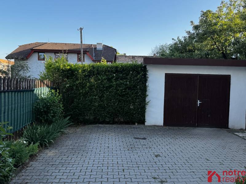 A family house in Lučenec with a garage, a paved courtyard, and greenery around the property.