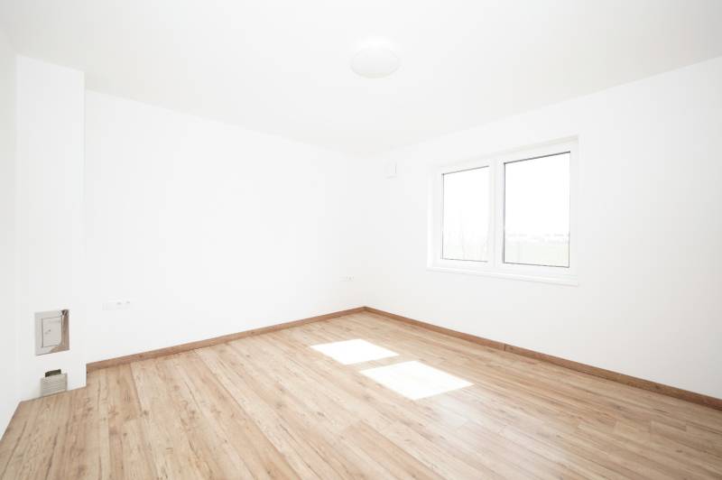 An empty room with a wooden floor and a large window in a family house.