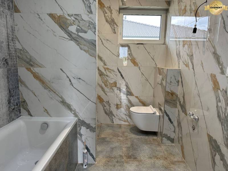 A bathroom in a family house tiled with a marble pattern, featuring a bathtub and a toilet.