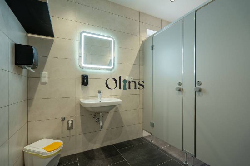 Modern office restroom with a mirror, sink, soap dispenser, and enclosed stalls.