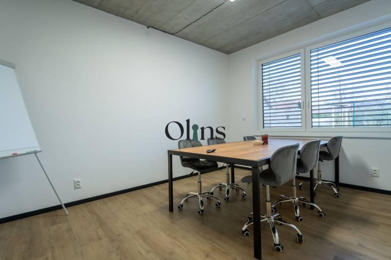 Office with a conference table, chairs, and a flipchart under a window with blinds.