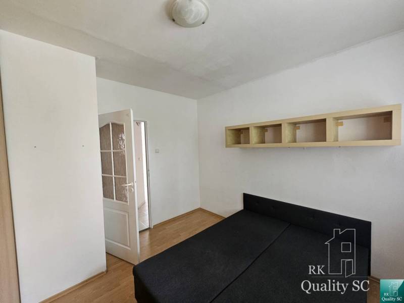 Bedroom in a two-room apartment with a bed, cabinet, and open door leading to the hallway.