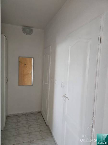 A hallway with a mirror in a 2-room apartment, white walls and doors, tiles on the floor.