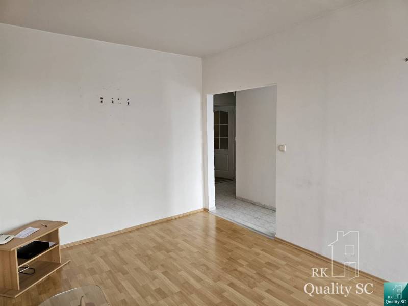 A room in a 2-room apartment with a wooden floor and white walls, with furniture.