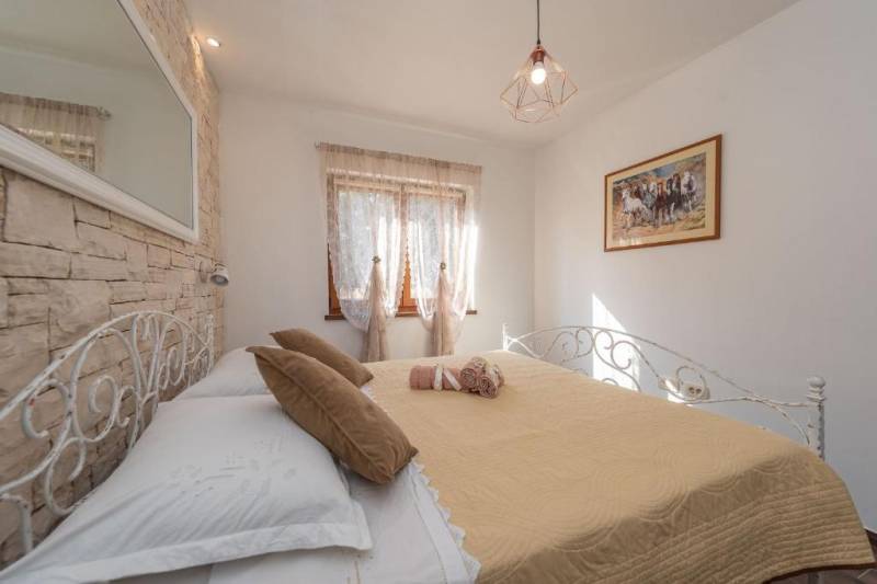 Bedroom in a family house with an iron bed, a painting on the wall, and stone cladding.
