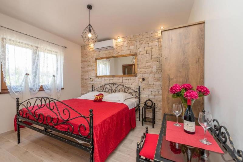 A bedroom in a family house with a metal bed, stone walls, and red accessories.