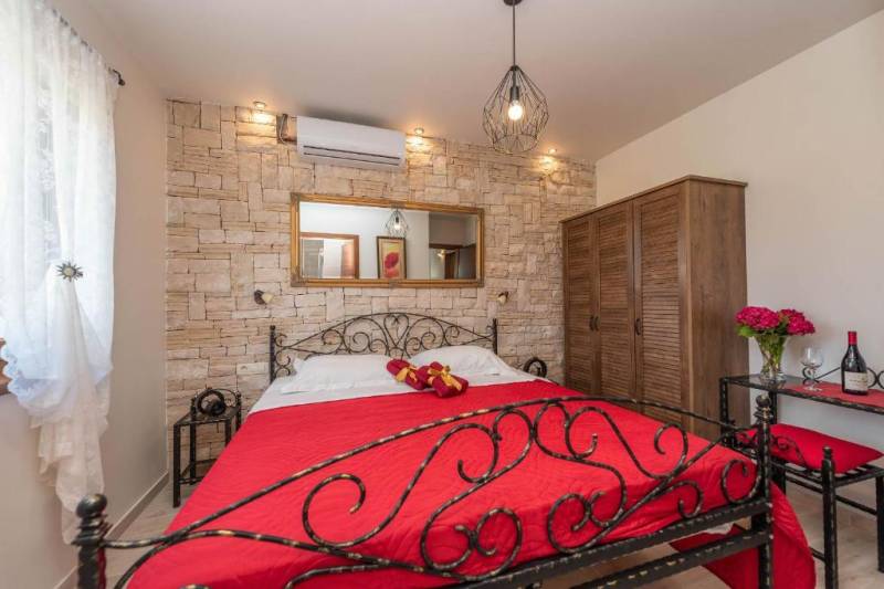 A bedroom in a family house with a stone wall, a metal bed, and a wooden wardrobe.