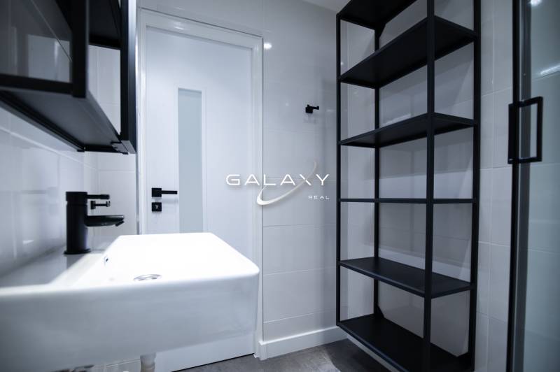 A minimalist bathroom with a white sink, black elements, and shelves in a 3-room apartment on Boriny Street.