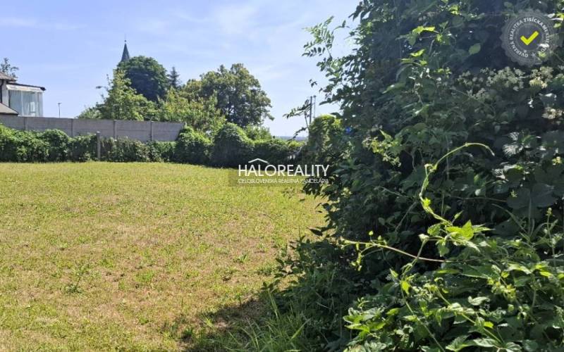 A plot for living in Smolenice, with maintained grass and fencing, bordered by greenery.