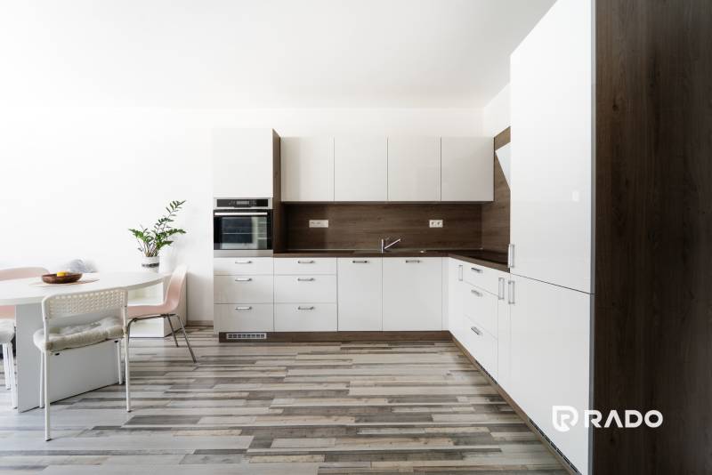 A kitchen in a 2-room apartment with a white kitchen unit and wooden floor.