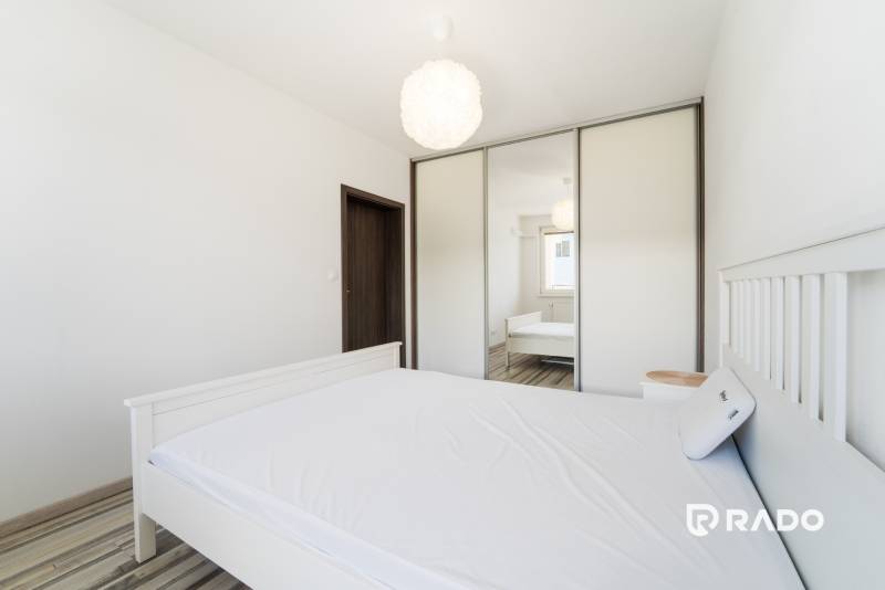 A bedroom in a two-room apartment with a white bed, a mirrored wardrobe, and a light interior.