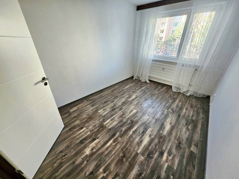 An empty room with laminate flooring and a large window in a three-room apartment.