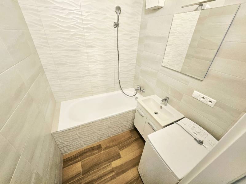 A bathroom in a 3-room apartment with a bathtub, sink, and washing machine.