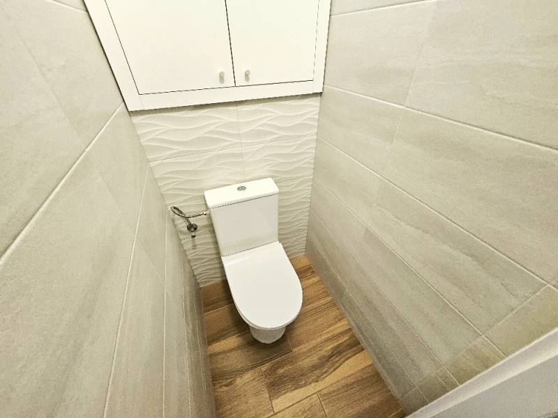 A bathroom in a 3-room apartment with wooden flooring and subtle wall tiles.