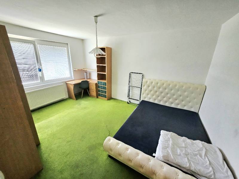 A room in a 3-room apartment with a bed, a table, and a green carpet.