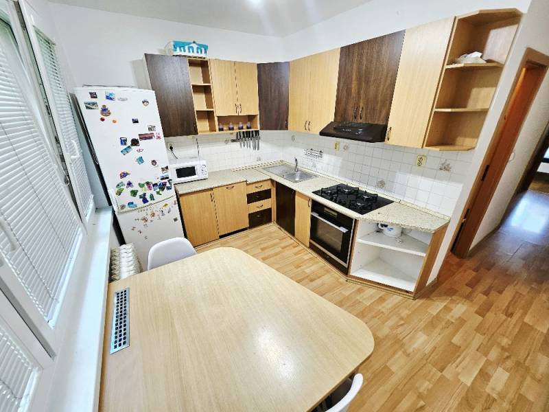A kitchen in a 3-room apartment with a stove, refrigerator, and wooden table.