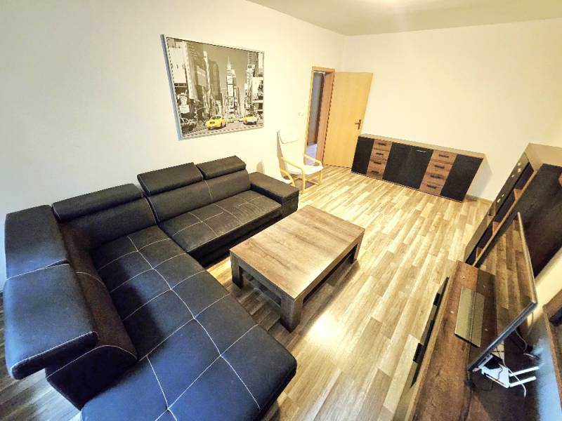 Living room in a three-room apartment with a black sofa and wooden furniture.