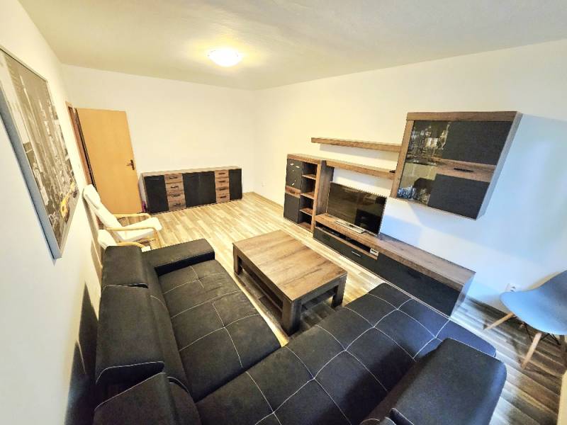 Living room in a 3-room apartment with a black sofa, furniture, and wooden flooring.