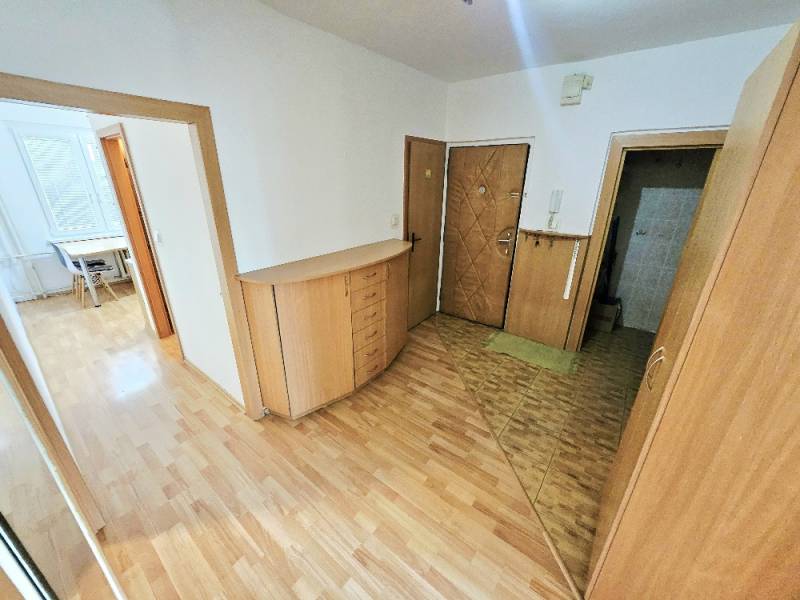 The hallway of a 3-room apartment with wooden floors and furniture, view towards the room.
