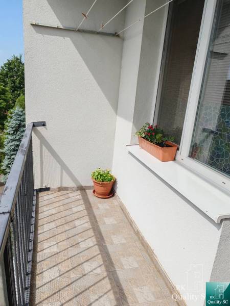 A balcony with flower pots belonging to a 3-room apartment, view of greenery.