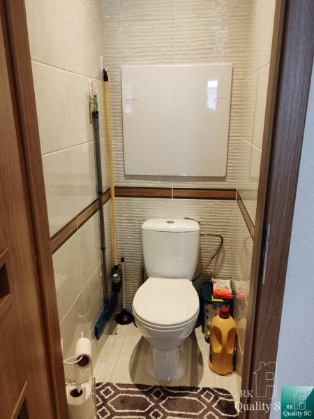 A toilet in a 3-room apartment with storage space for cleaning supplies.