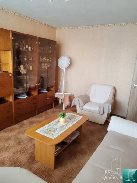 Living room in a three-room apartment with wooden furniture and a white armchair.