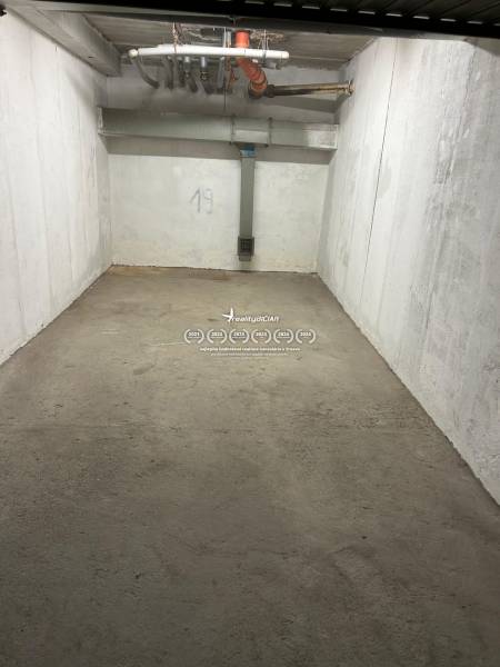 Closed garage space with a concrete floor and white walls, number 19, pipes on the ceiling.
