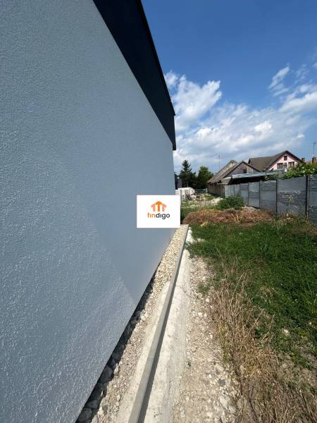 The wall of a family house in Žihárec with an adjacent plot of land under the blue sky.