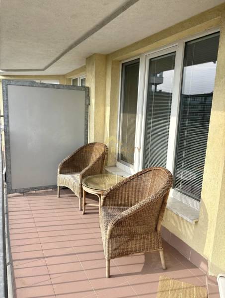 A balcony of a 2-room apartment with two rattan chairs and a table.