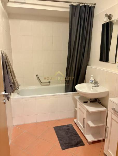 A bathroom in a 2-room apartment with a bathtub, a sink, and a shower curtain.