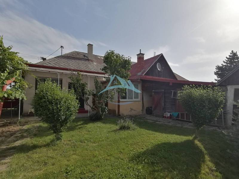 A family house in Hrkovce with a garden, shrubs, and a wooden shelter.