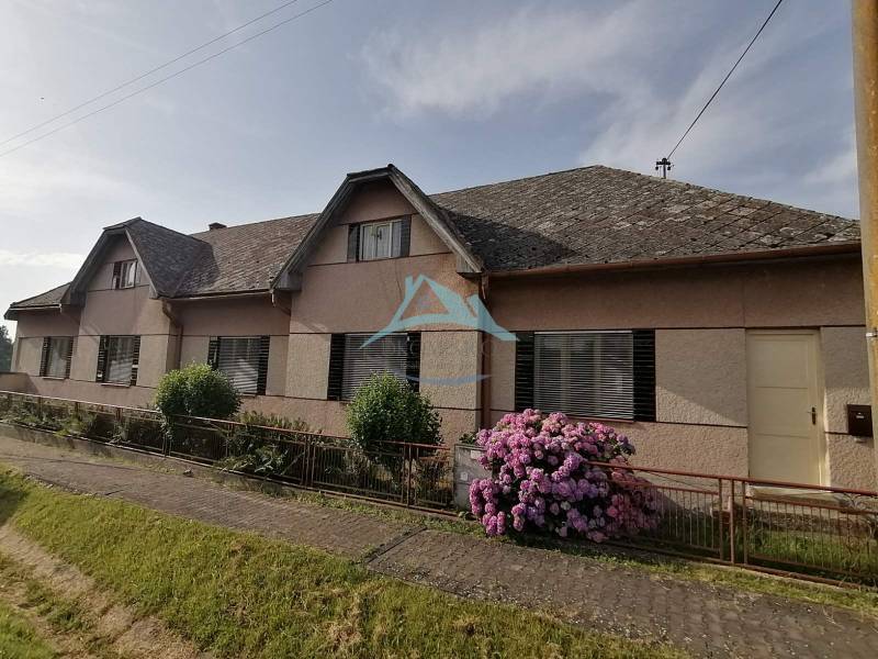 A family house in Hrkovce with flowers in front of the fence and a sloped roof.