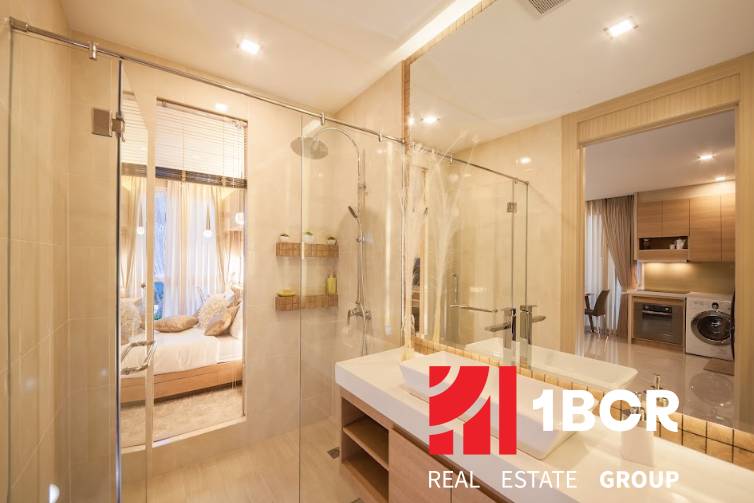 A bathroom in a 2-room apartment with a shower and a sink, leading to the bedroom.