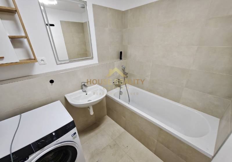 Bathroom in a 3-room apartment with a bathtub, sink, and washing machine, beige tiles.