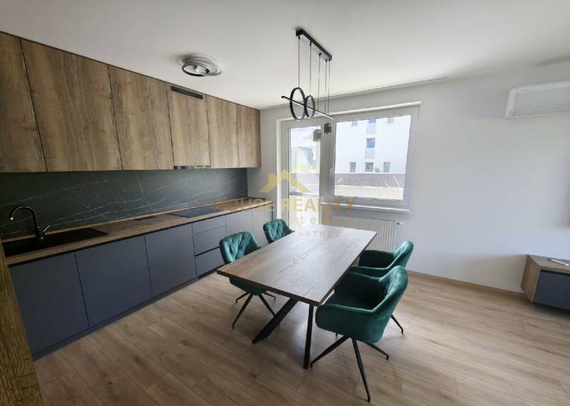 A kitchen in a 3-room apartment with wooden and dark cabinets, a dining table, and emerald chairs.