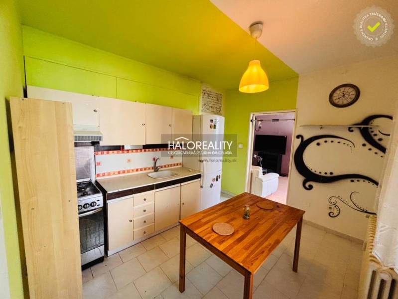 A kitchen with green walls, white cabinets, and a dining table in a three-room apartment.