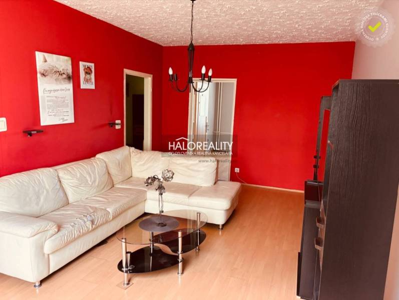 Living room in a 3-room apartment with a white couch, red walls, and a glass table.