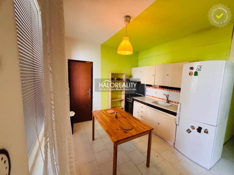 A kitchen in a 3-room apartment with a green wall, a wooden table, and white cabinets.