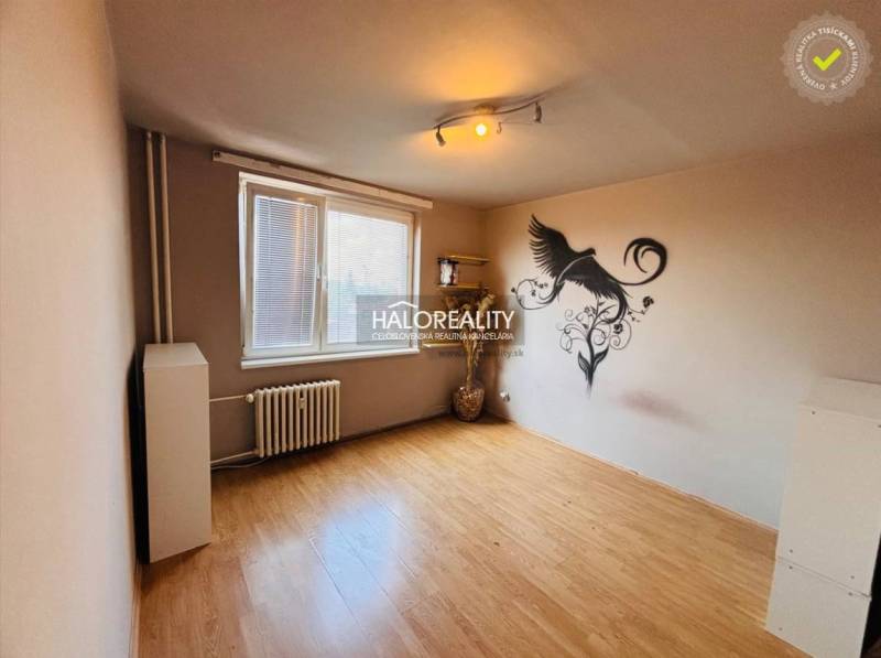 A room in a 3-room apartment with wooden flooring and a wall decoration of a bird.