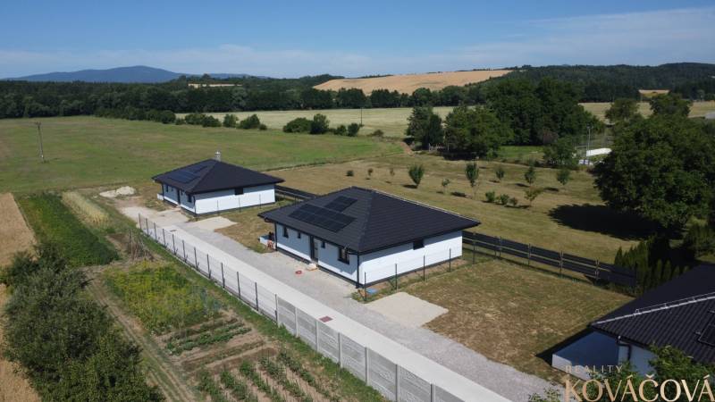 Family houses in Podlužany with modern roofs and solar panels in the field.